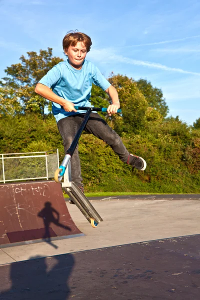 Мальчик прыгает на скутере в скейт-парке через рампу — стоковое фото