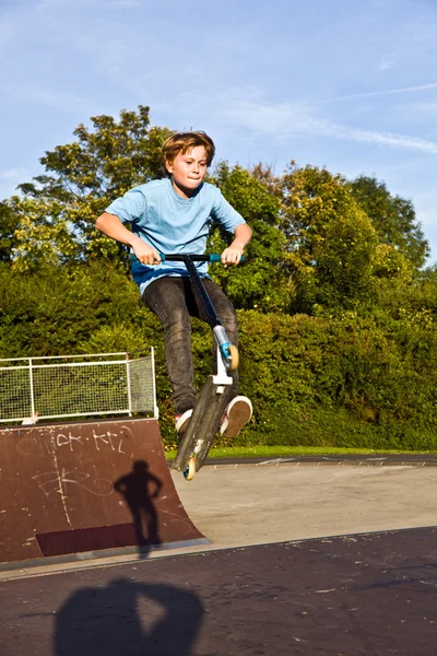男孩用滑板车滑板公园在跳跃一个坡道 — 图库照片