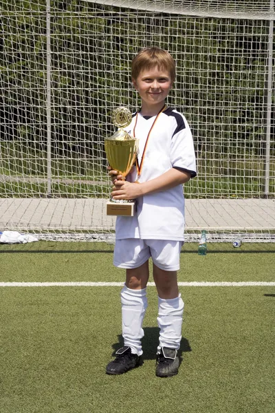 Young boy in soccer dress presents proud the cup — Zdjęcie stockowe