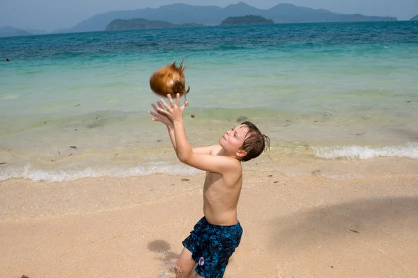 Pojke leker med en kokosnöt på en vacker strand — Stockfoto