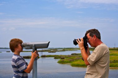 Father takes a picture of his son looking thru a telescope clipart