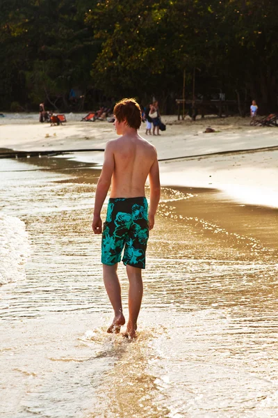 Fiatal fiú sétált a gyönyörű tengerparton háttérvilágítás — Stock Fotó