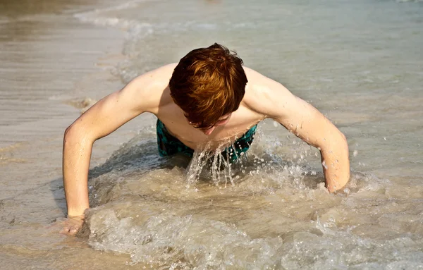 Pojken i bathingsuit ligger på stranden och njuter av saltwa — Stockfoto