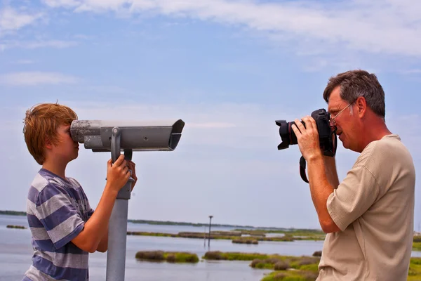 Padre toma una foto de su hijo mirando a través de un telescopio — Foto de Stock