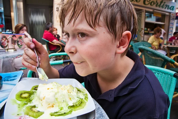 Niño disfruta de helado sentado al aire libre en una mesa —  Fotos de Stock