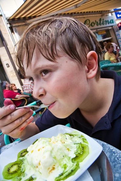 Child enjoys ice cream sitting outdoors at a table — Stock Photo, Image