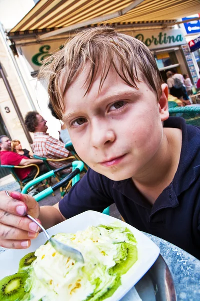 Criança gosta de sorvete sentado ao ar livre em uma mesa — Fotografia de Stock