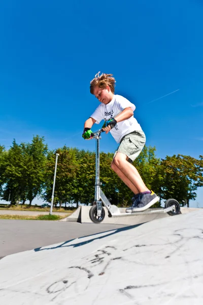 Menino se diverte no parque de skate com sua scooter — Fotografia de Stock