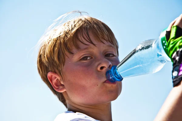 Menino está suando e sussurrando e bebe água mineral — Fotografia de Stock