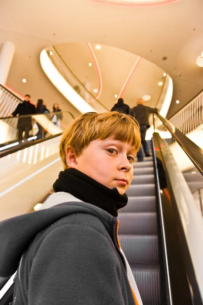 Niño en la escalera en movimiento se ve seguro de sí mismo y sonríe —  Fotos de Stock