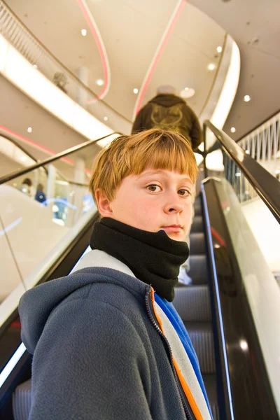Niño en la escalera en movimiento se ve seguro de sí mismo y sonríe —  Fotos de Stock