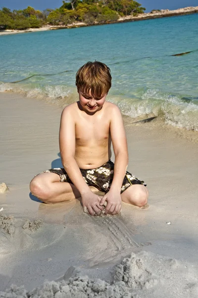Fiú játszik a tengerparton homok és épület adatok — Stock Fotó