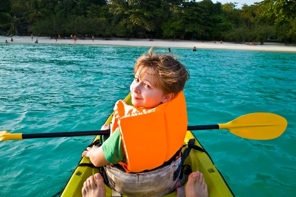 Boy paddles in a canoe at the ocean with safety west — Stock Photo, Image