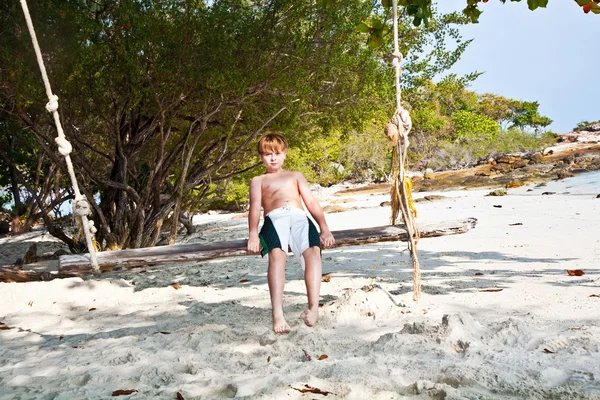 Хлопчик сидить на гойдалці на пляжі під деревами — стокове фото