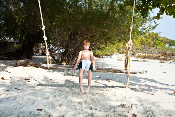 Çocuğu salıncakta ağaçların altında sahilde oturuyor. — Stok fotoğraf