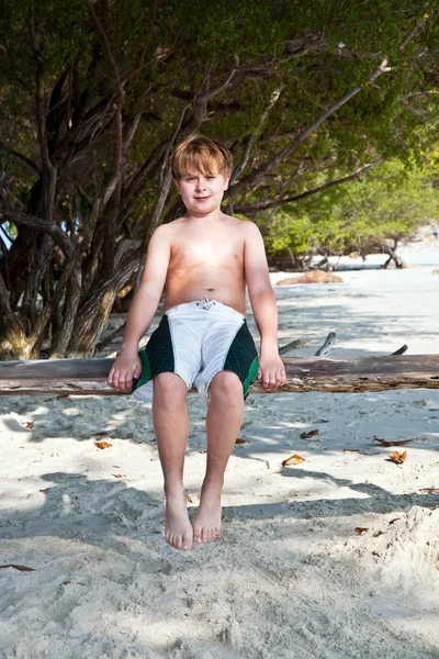 Niño sentado en un columpio en la playa bajo los árboles — Foto de Stock