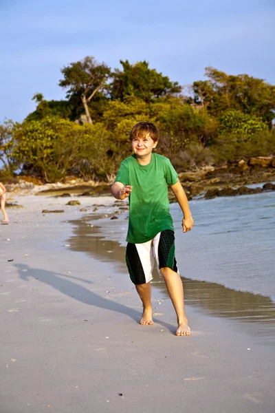 Szczęśliwy młody chłopiec biegnie wzdłuż pięknej plaży — Zdjęcie stockowe