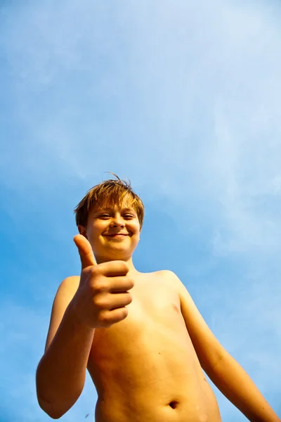 Felice sorridente giovane ragazzo con sfondo cielo blu dà fingersig — Foto Stock