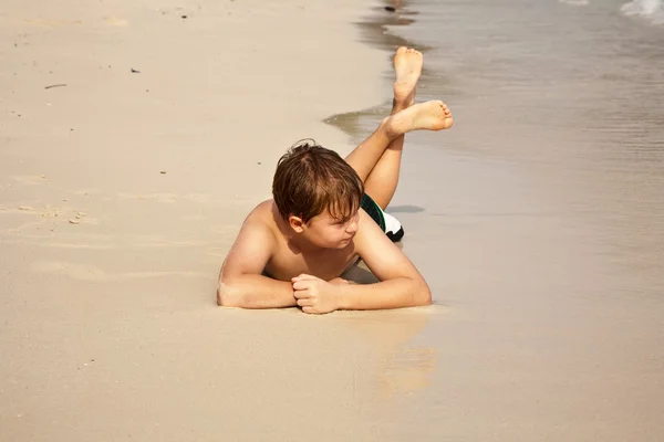 Menino iy deitado na praia e apreciando o calor da água — Fotografia de Stock