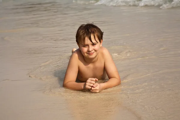 Хлопчик лежить на пляжі і насолоджується теплом води — стокове фото