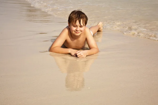 Menino iy deitado na praia e apreciando o calor da água — Fotografia de Stock