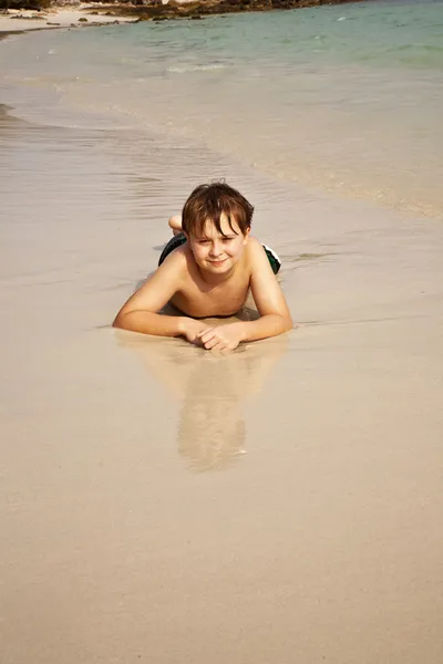 Pojke iy ligger på stranden och njuter warmness av vattnet — Stockfoto
