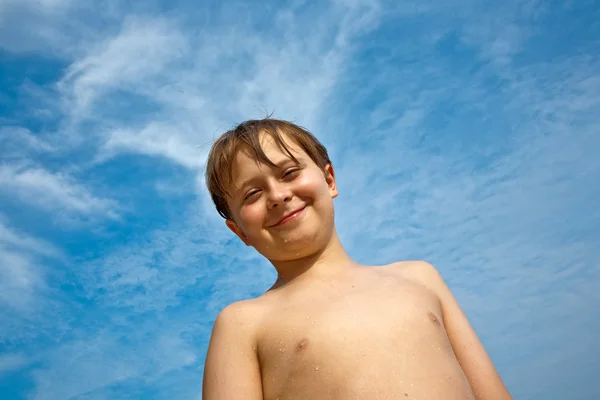 Glad ung pojke med brunt hår och ögon på stranden ler — Stockfoto