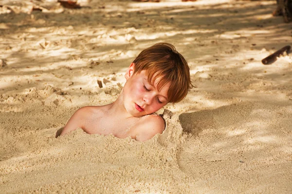 Счастливый мальчик, покрытый мелким песком на пляже — стоковое фото