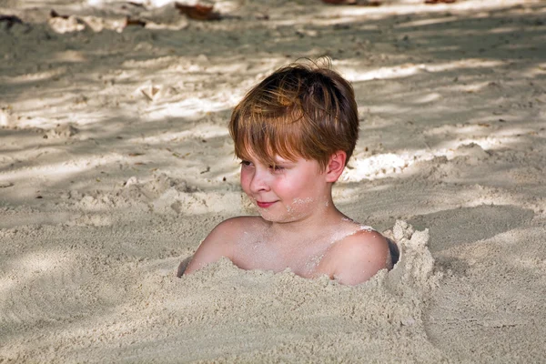 Glad ung pojke omfattas av fin sand på stranden — Stockfoto