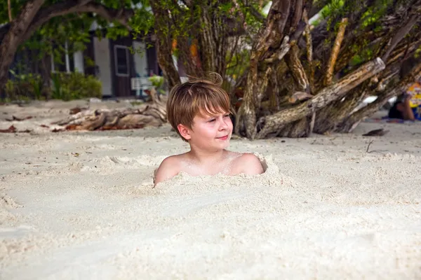 Heureux jeune garçon couvert de sable fin à la plage — Photo