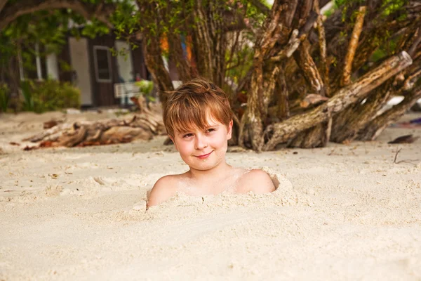 Щасливий молодий хлопчик вкритий дрібним піском на пляжі — стокове фото