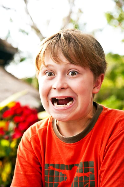 Fiatal fiú ül egy tengerparti étteremben vicces arcokat vág — Stock Fotó