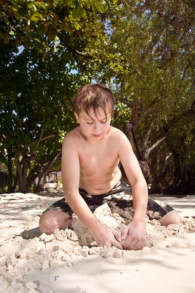 Niño feliz está cavando en la arena de la playa y construc —  Fotos de Stock