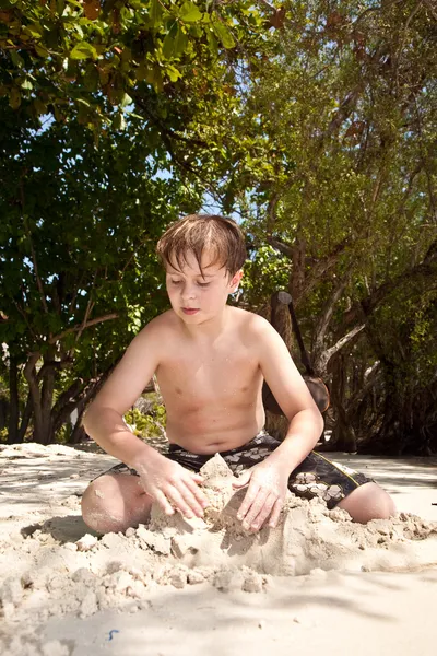 Šťastný chlapec je kopání v písku na pláži a volili — Stock fotografie