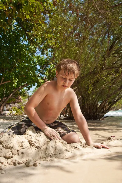 Jovem feliz está cavando na areia da praia e construindo — Fotografia de Stock