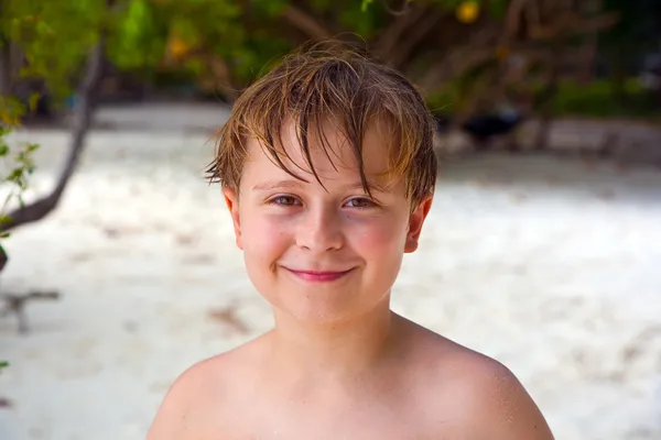 Niño feliz con el pelo mojado en la playa sonríe y se ve muy auto — Foto de Stock