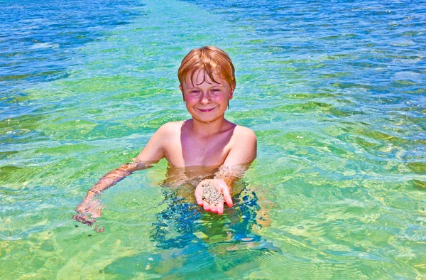 Chlapec v oceánu ukazuje čistého písku na ruce — Stock fotografie