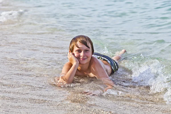 Chlapec se těší, ležící na pláži v příboji — Stock fotografie