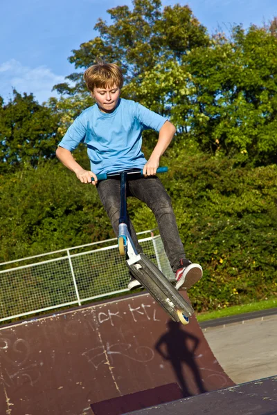 Αγόρι άλματα με σκούτερ στο skate park πέρα από μια κεκλιμένη ράμπα — Φωτογραφία Αρχείου