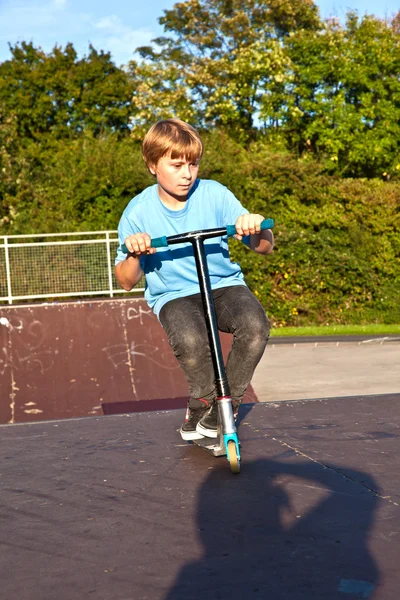 Chłopiec skacze z skuter w skate parku na ziemi — Zdjęcie stockowe
