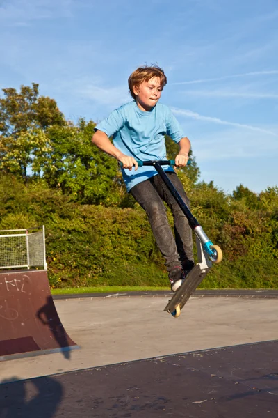 Garçon saute avec scooter au skate park sur une rampe — Photo
