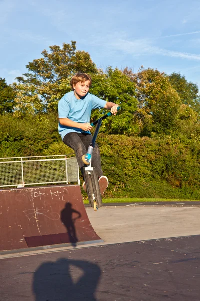 Мальчик прыгает на скутере в скейт-парке через рампу — стоковое фото
