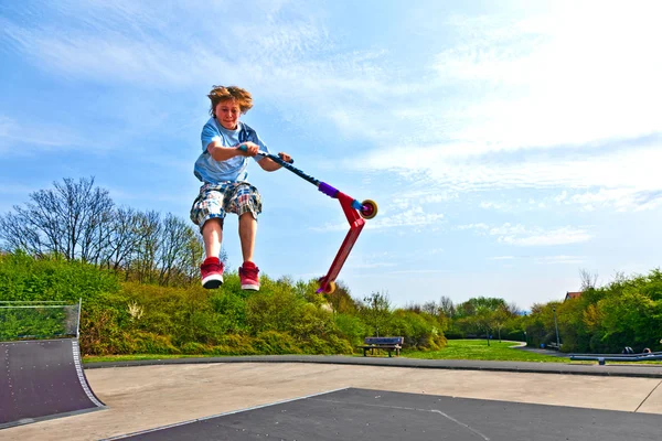 Ragazzo sta saltando con uno scooter sopra una colonna vertebrale nel parco skate — Foto Stock