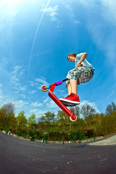 Pojken hoppar med en skoter över en ryggrad i skate parc — Stockfoto