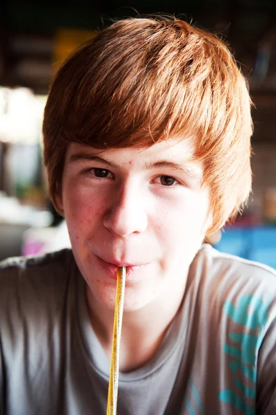 Мальчик с рыжими волосами хочет пить и пьет с соломинкой — стоковое фото