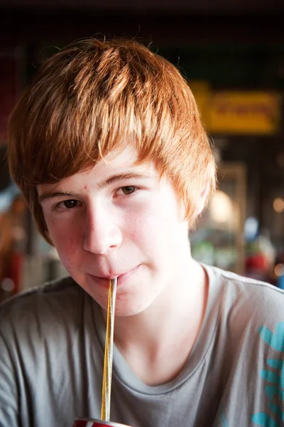 Мальчик с рыжими волосами хочет пить и пьет с соломинкой — стоковое фото