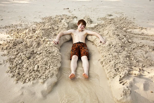 Хлопчик лежить у піщаному ліжку на красивому повному пляжі — стокове фото