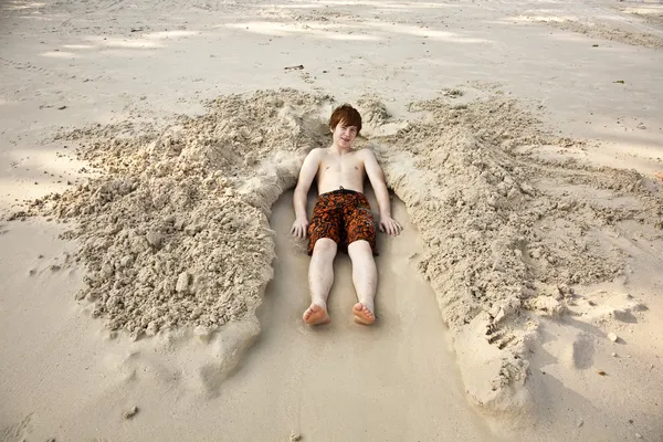 Мальчик лежит в песчаной постели на прекрасном пляже — стоковое фото