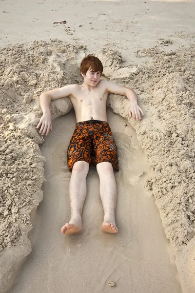 Chico está acostado en una cama de arena en la hermosa playa —  Fotos de Stock