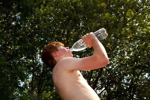 Giovane ragazzo beve acqua da una bottiglia nel calore — Foto Stock